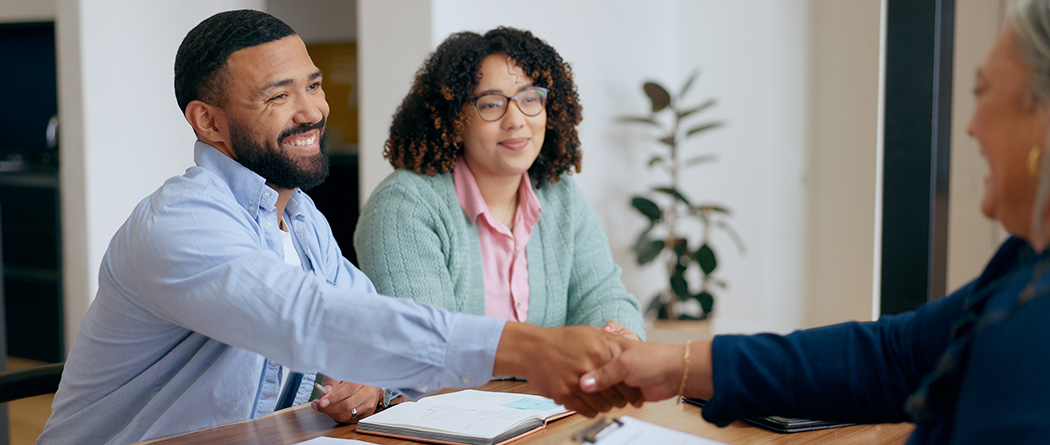 Satisfied couple at loan closing shakes hands with lender