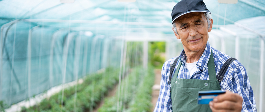 Produce farmer in greenhouse viewing his credit card