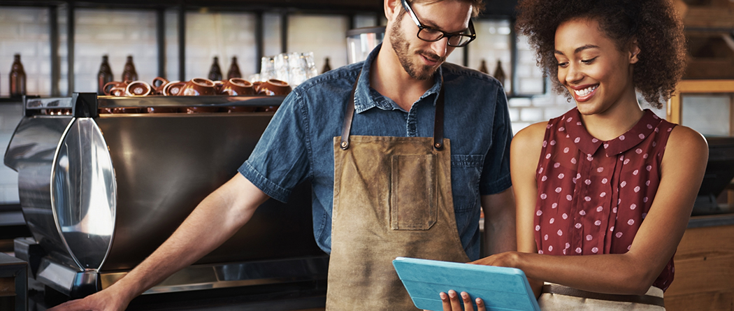 Coffee shop manager looks over financials on device with employee