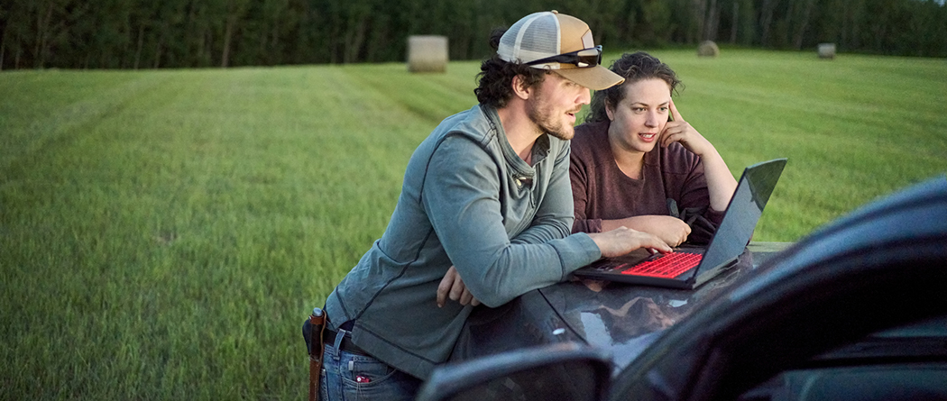 Young man and woman working from laptop in hay field